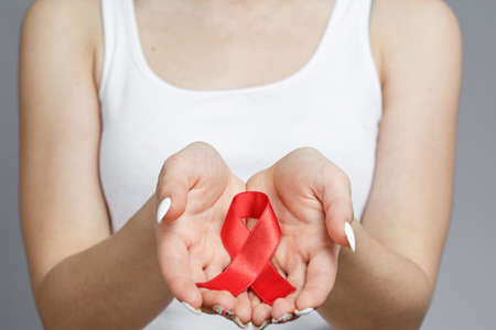 female hands holding red AIDS awareness ribbon, healthcare and medicine concept