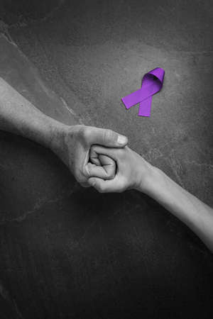 Hands holding purple ribbons top view on gray wooden background. Alzheimers disease, epilepsy, fibromyalgia awareness, world cancer day. black and white. symbol of fighting child abuse.の写真素材