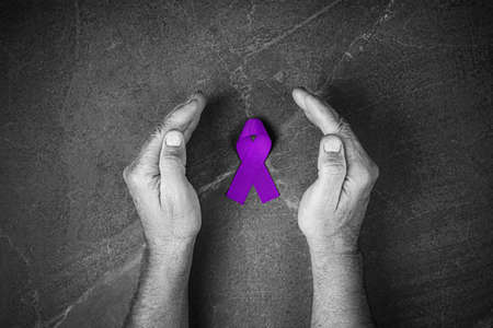 Hands holding purple ribbons top view on gray wooden background. Alzheimers disease, epilepsy, fibromyalgia awareness, world cancer day. black and white. symbol of fighting child abuse.の写真素材