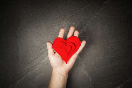 red heart in hands on gray background, the concept of love and care for loved ones and needy. February 14th conceptの写真素材