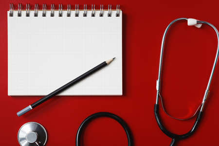 Stethoscope, notebook and pencil on the red table, the concept of health and medicineの写真素材