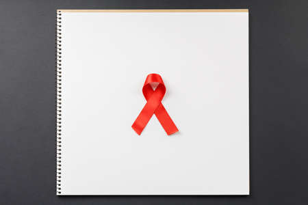 red AIDS ribbon on notebook lying on dark table top view, world day to fight cancer and aids. hiv supportの写真素材
