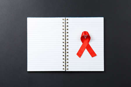 red AIDS ribbon on notebook lying on dark table top view, world day to fight cancer and aids. hiv supportの写真素材