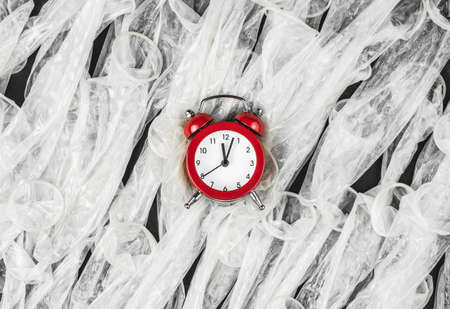 red alarm clock with condoms on black background, flat lay, concept of fight against HIV and aidsの写真素材
