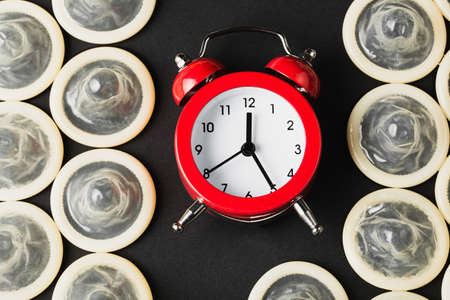 red alarm clock with condoms on black background, flat lay, concept of fight against HIV and aidsの写真素材