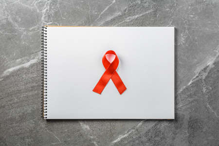 red aid ribbon on empty notebook on gray marble table top view, symbol of the fight against cancer, hiv and aids, flat lay. lot of free space.の写真素材