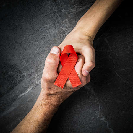 AID red ribbon in hand on dark gray marble background, symbol of the fight against HIV, AIDS and cancer. concept of helping those in needの写真素材
