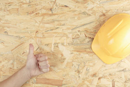 construction helmet in hands on a wooden board top view. osb board as backgroundの写真素材