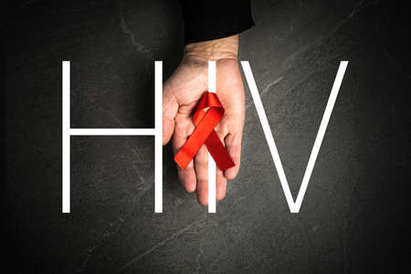 red ribbon in hand words HIV on dark gray background, symbol of the fight against AIDS and cancer. concept of helping those in needの写真素材