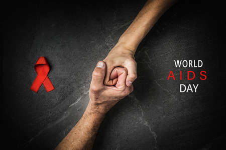 red ribbon hands together words world AIDS day on dark gray background, symbol of the fight against HIV, cancer. concept of helping those in needの写真素材