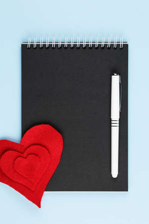 red heart on black notebook and blue background top view, symbol of love, peace, health and help to those in need vertical viewの写真素材