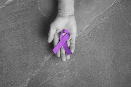 Hands holding purple ribbons top view on dark gray background. Alzheimers disease, epilepsy,...