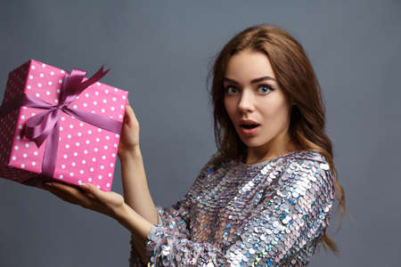 girl in a shiny New Years dress with a gift box with a heart. Birthday photo concept.
