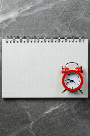Spiral notebook with red alarm clock on marble table. Notepad goals plans dreams, make to do list for new year concept of diary, planning. Flat lay, top view, mockup.の写真素材