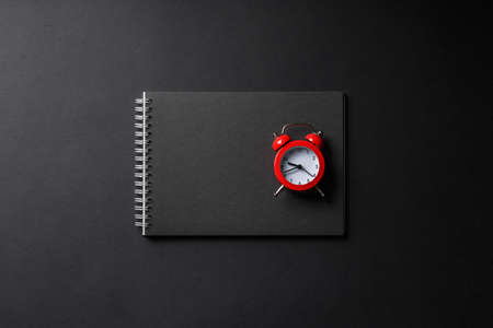 open black notebook with red alarm clock on black background top view, school notepad on a dark table, office desk flat layの写真素材