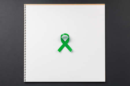 green cancer ribbon on notebook lying on dark table top view, world day to fight cancer and support....