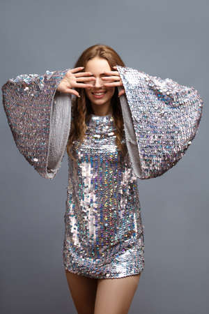 Beautiful girl in a shiny dress closes her eyes on gray background posing in the studio.の写真素材