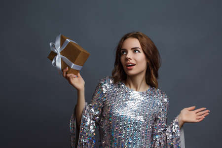 girl in a shiny New Years dress with a gift box with a heart. Birthday photo concept.の写真素材