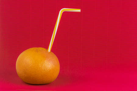 Fresh orange with straw inside on pink background. cocktail day concept. diet drink.の写真素材