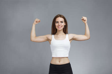 Portrait of pretty feminist woman shows her muscular arms proud from girl power and ready to face any challenges. strong lady fight with confident. Shows strength with raised hand, gray backgroundの写真素材