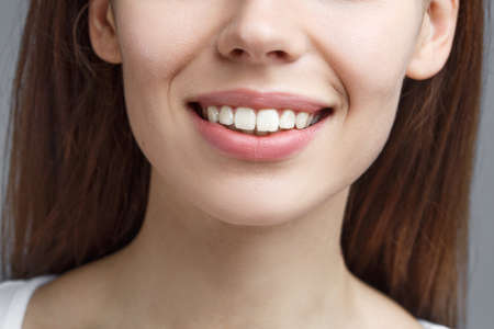 closeup beautiful smile and healthy teeth. beautiful young girl on gray background