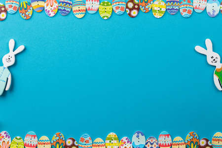 Easter background with painted eggs and rabbits on blue background top view, festive background with...