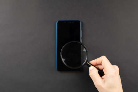 search in the phone with a magnifying glass in the hands on a black background, top view. search engine concept. spying mobile smart phoneの写真素材