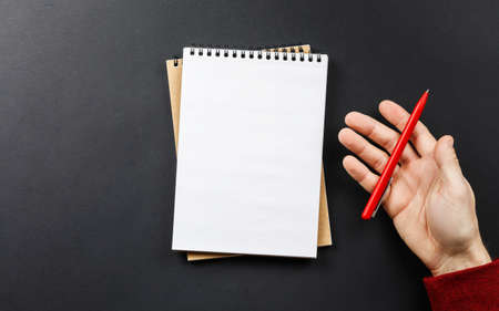 open notebook with black pen in hands on black background top view, school notepad and male hands in...