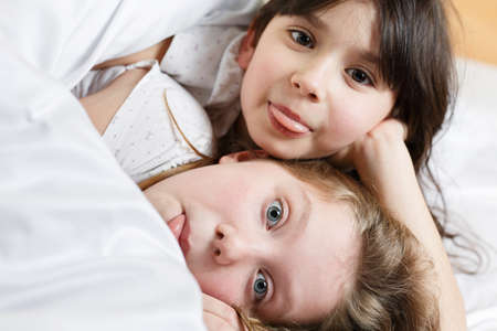 sisters playing in the bedroom, two cute little girls fooling around on the bedの写真素材