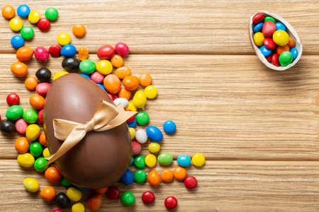 easter composition top view. chocolate eggs with colorful candies on wooden background flat lay with space for textの写真素材