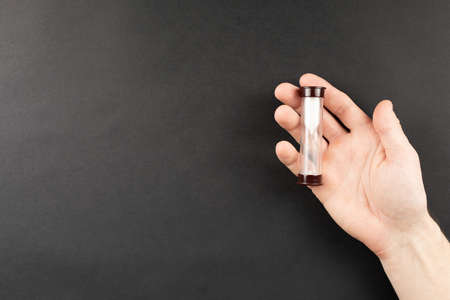 hourglass in hand on black background, top view. time runs away, flat lay. sandglass on palms. time...