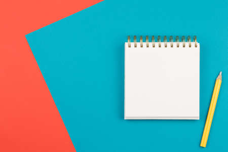 open notebook with a yellow pencil on two-color background blue and coral pink, top view, spiral notepad with blank sheet on the table flat layの写真素材