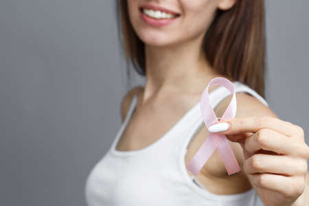 Woman with pink ribbon on gray background, closeup. Breast cancer awareness conceptの写真素材