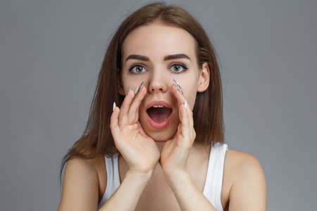 Attention. Close up portrait of heerful young woman screaming while  holding hands near her open...