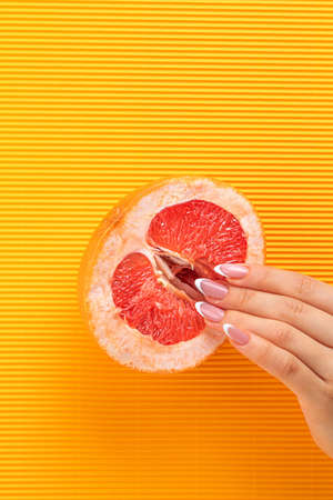 fingers on grapefruit on striped yellow background. Sex concept. sexy fruit composition. Vagina symbol.の写真素材