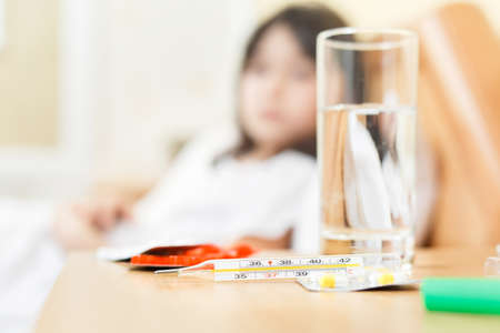 little girl is sick and lies in bed, next to them are tablets with a gradus. The child has a fever,...