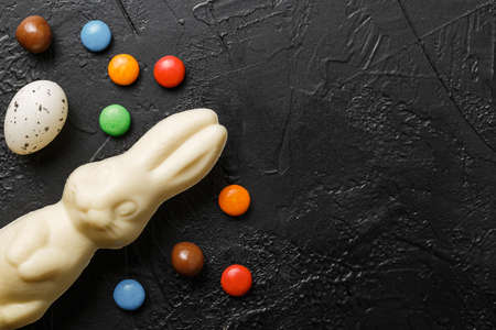 easter composition top view. white chocolate bunnies with colorful candies on black background flat...