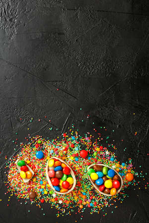 easter composition top view. chocolate eggs with colorful candies on black background flat lay with...