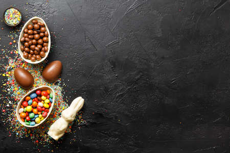 easter composition top view. chocolate eggs with colorful candies on black background flat lay with...