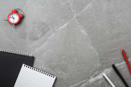 black notebook with pen and alarm clock on gray marble table top view. stone office desk with spiral...