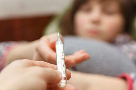 child is measured by the temperature of a thermometer, a cold and the flu is at home with a high temperature, the doctor checks the patient, the temperature is 38 on a thermometerの写真素材