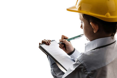 boy in a yellow construction helmet holding paper with pen on white isolated background, young engineer architect backlitの写真素材