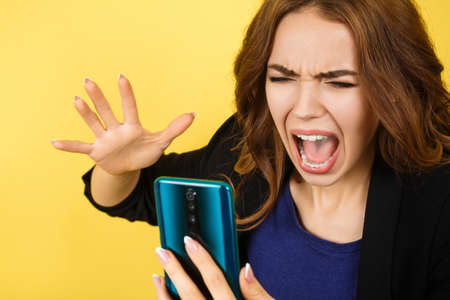 Angry woman shouting on smartphone, isolated on yellow backgroundの写真素材