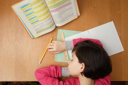 Little Asian schoolgirl fell asleep while doing homework at the desk at home. In the evening....