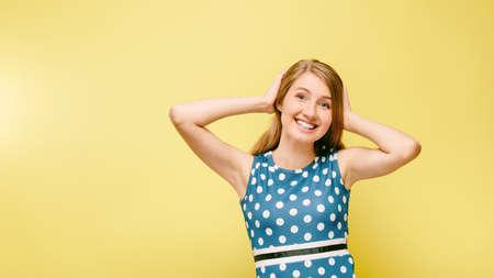cheerful teen girl in pea dress on yellow background holding on to her hair diluting elbows, model in studio on yellow backgroundの写真素材