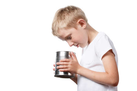 little child is looking in a tin can, starving boy is looking to eat, photo is isolated on a white backgroundの写真素材