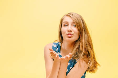 beautiful teen girl in pea dress on yellow background holds palm near face, model in studio on...