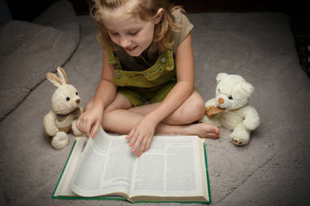 Beautiful little girl read book with her favorite toy on a soft plush blanketの写真素材
