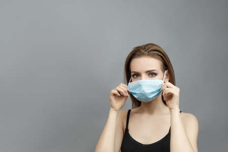 Beautiful woman put on medical mask on a gray background studio photo colds and flu.の写真素材