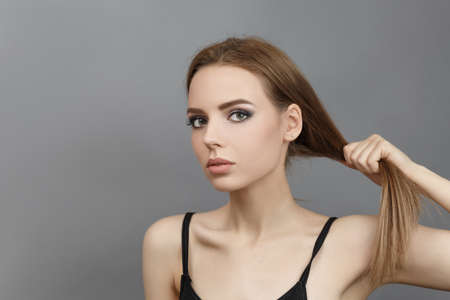 Beautiful girl holds hair with hands on a gray background.の写真素材
